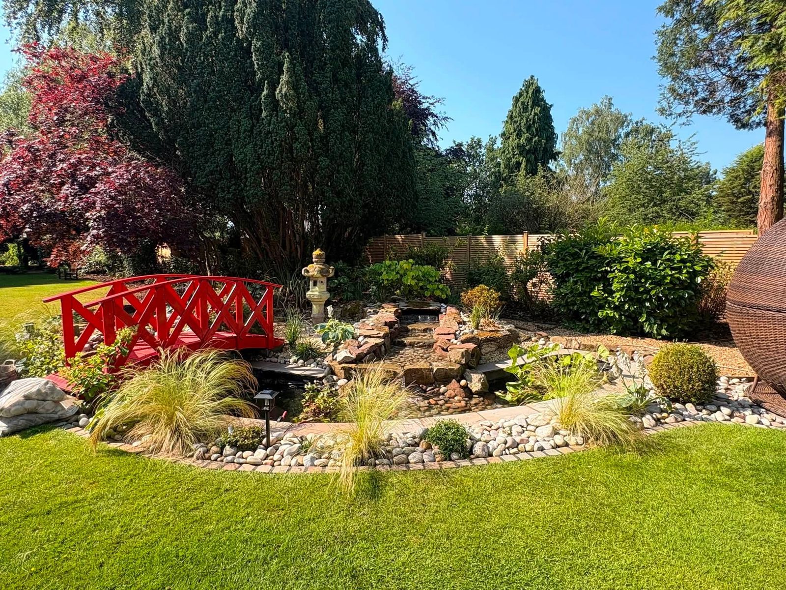 Japanese-inspired garden with red bridge and water feature, landscaped by DB Landscapes Ltd in Stockport